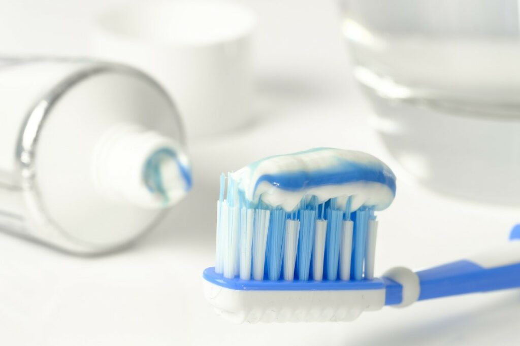 Modrý kartáček na zuby s nanesenou pastou na zuby, vedle bílá tuba s pastou - jsme připraveni na čištění.